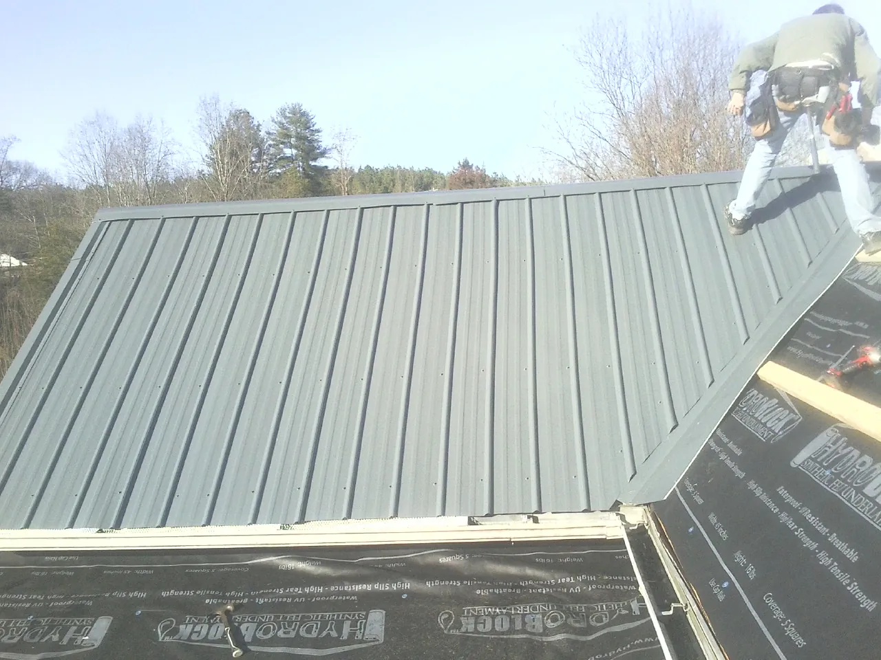 Crew installing dark green standing seam panels over synthetic underlayment in Federal Way
