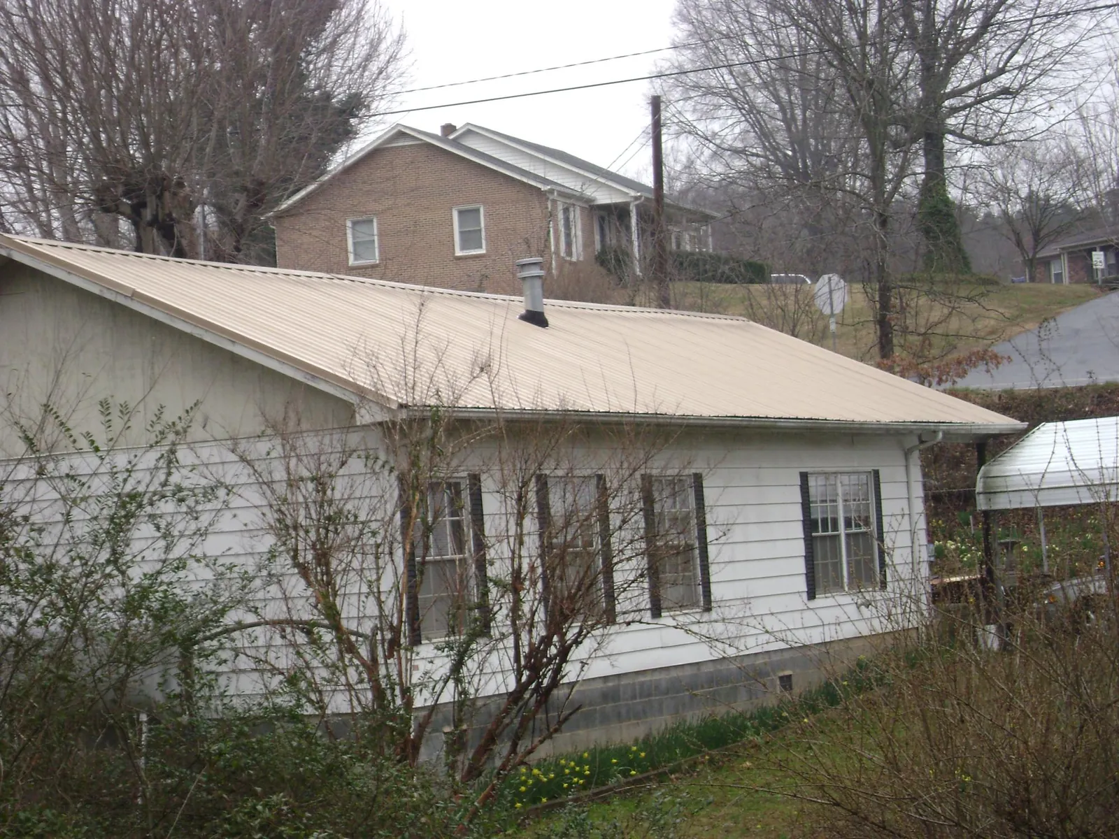 Tan metal roof on a white sided house set into a hillside — Commercial Roofing by Roofing Brothers in Federal Way